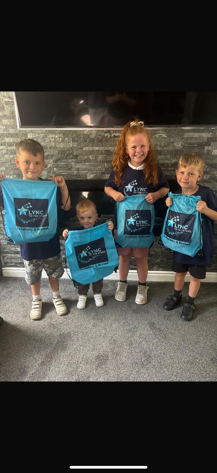 Four children holding their Lync to the Stars drawstring bags