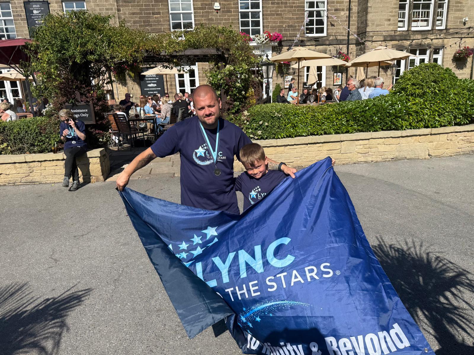 An adult and child holding the Lync to the Stars banner on the walk