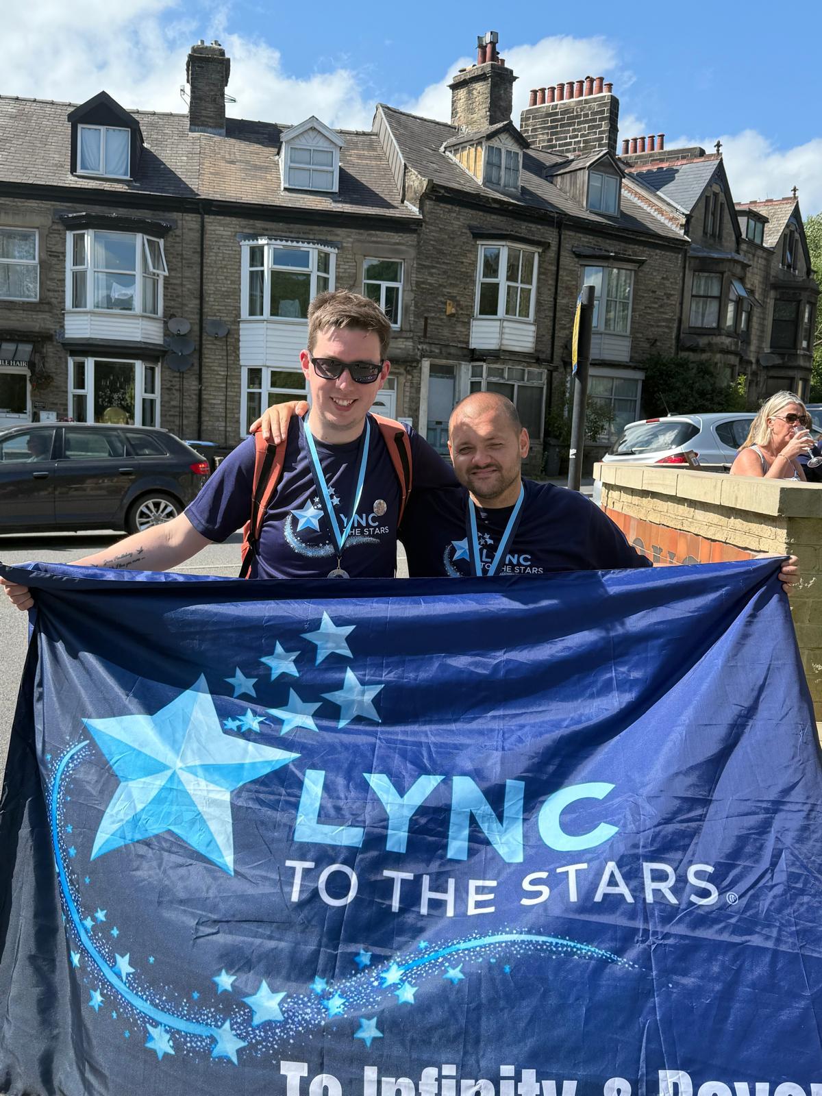 Two friends in Lync to the Stars t-shirts holding the banner together