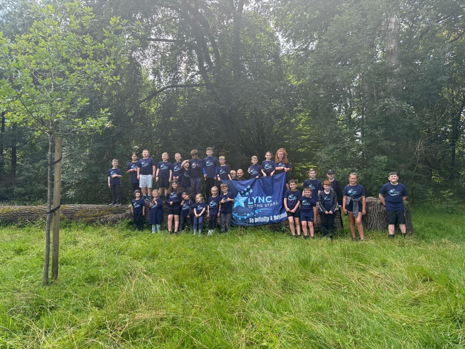 Children holding the Lync to the Stars banner on a woodland log