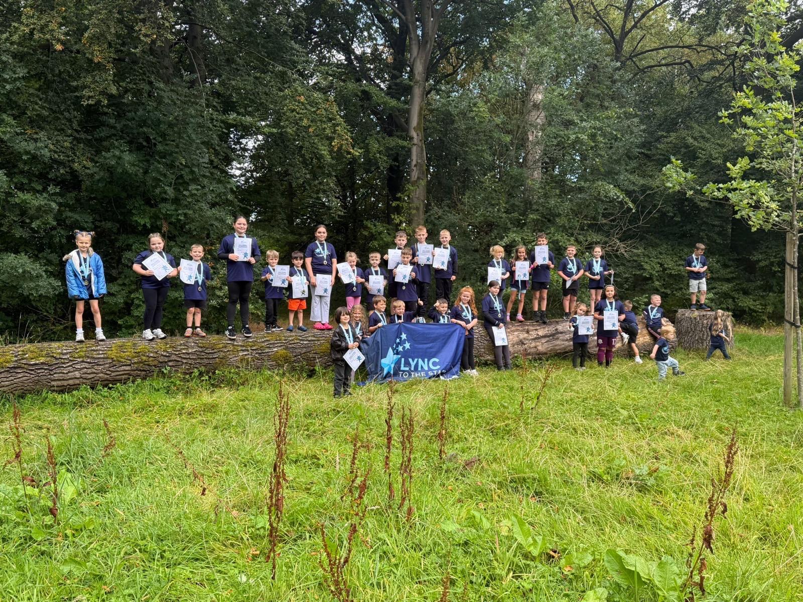 Children holding their certificates and the Lync to the Stars banner in the woodland