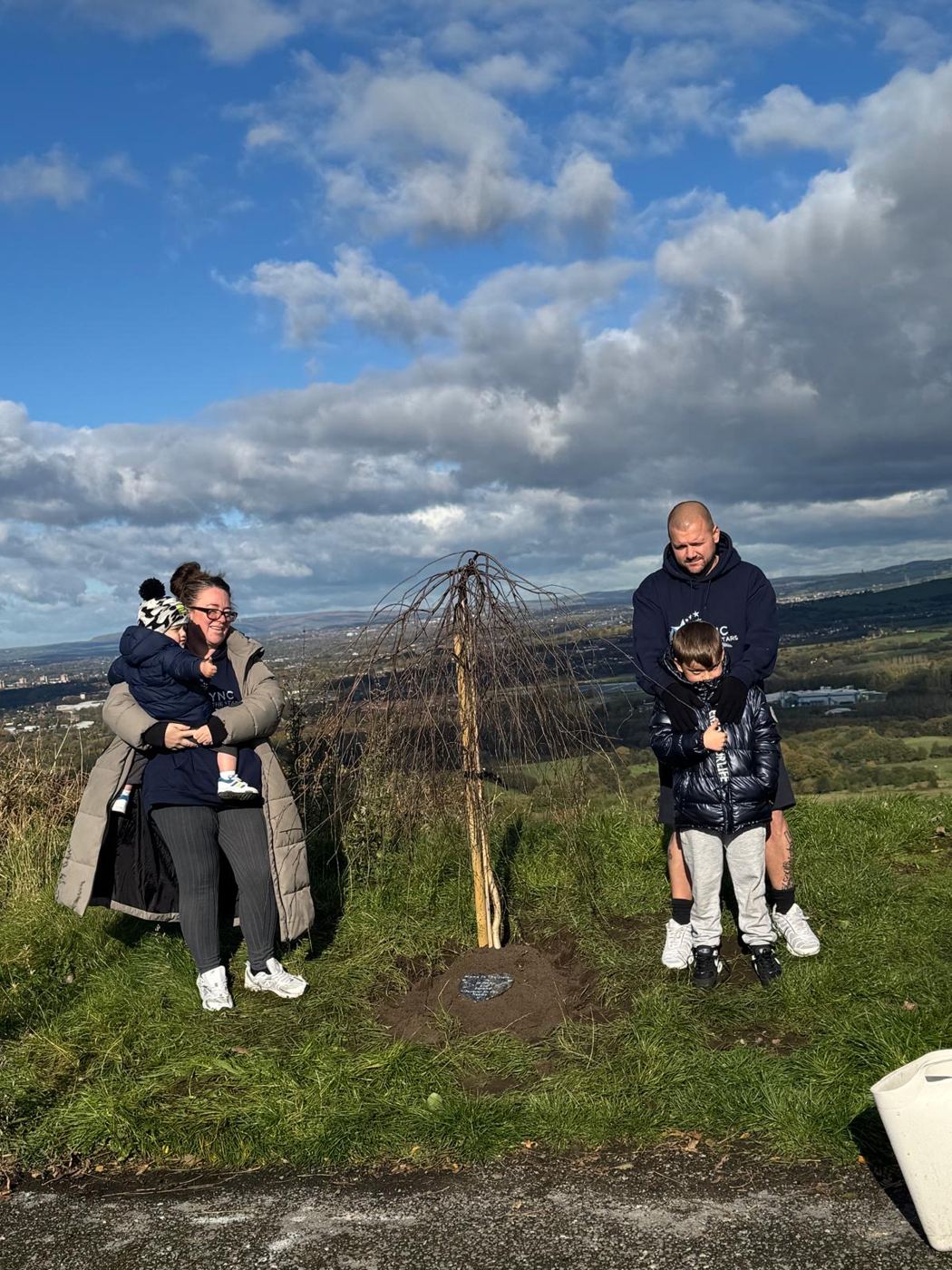 Family standing either side of Lync's Tree on a sunny day