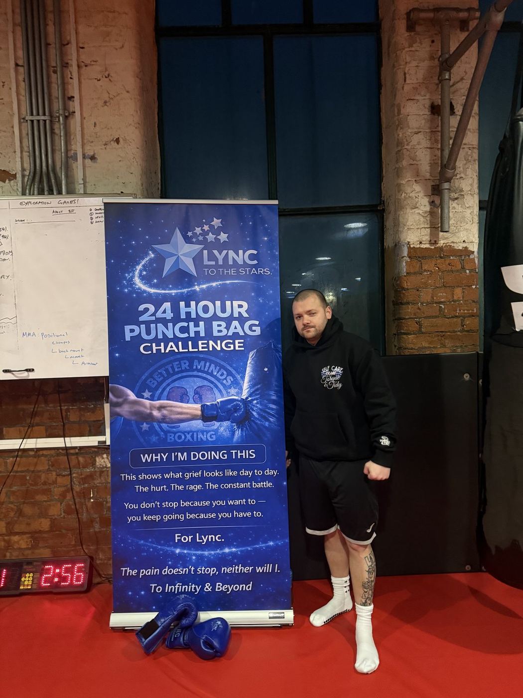 Lee standing beside the 24-Hour Punch Bag Challenge banner in the gym
