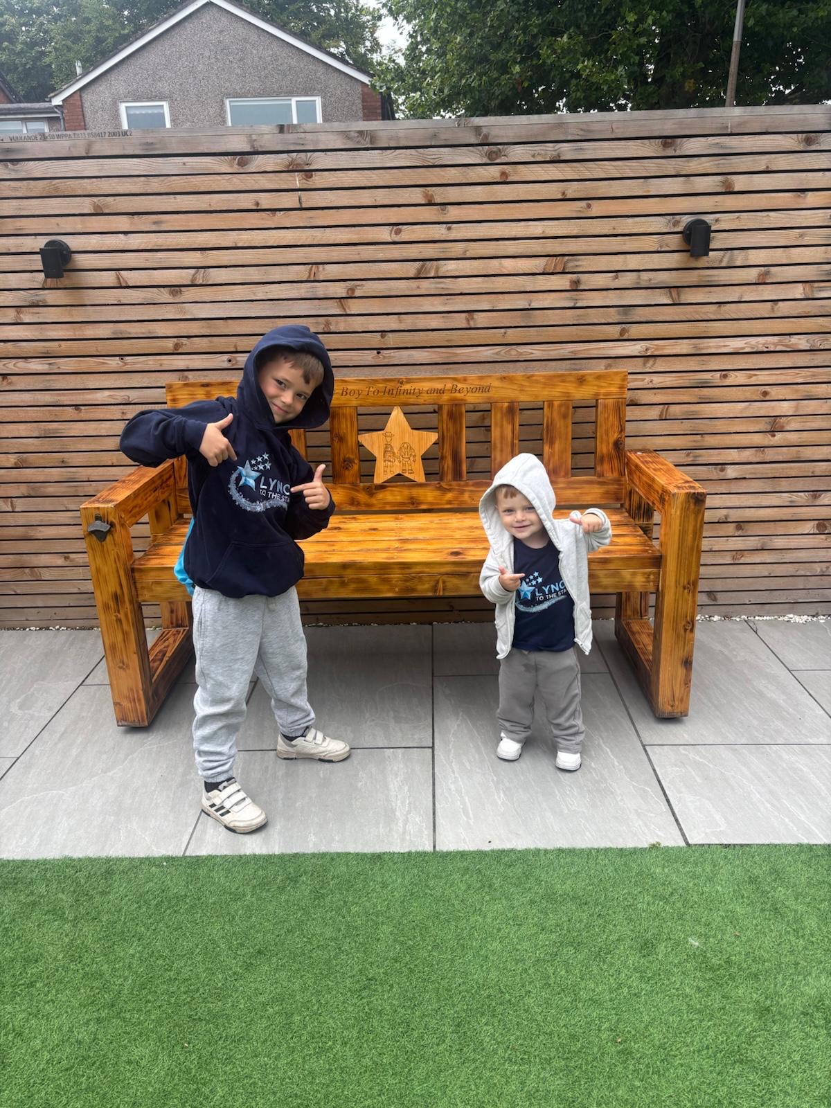 Two young children in Lync to the Stars tops standing proudly beside Lync's Bench