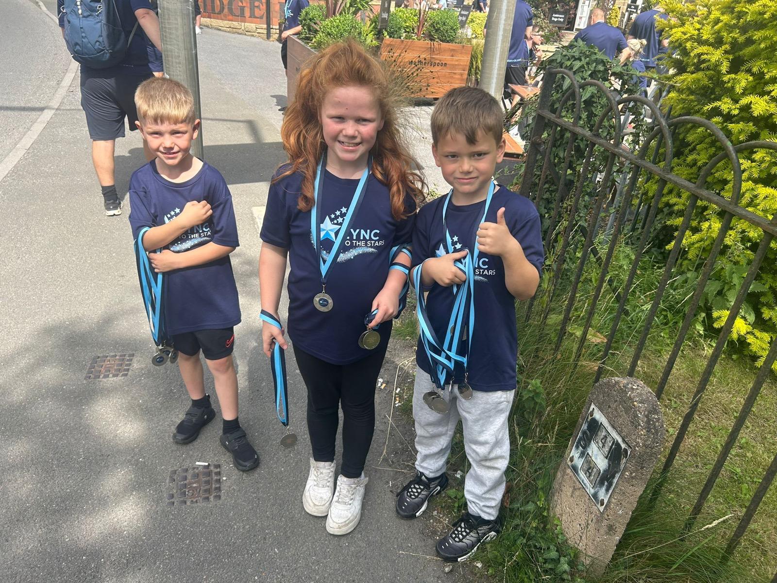 Three young walkers proudly showing their medals after completing Lync's Walk